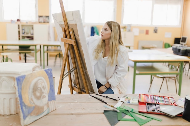Blonde jeune femme assise dans un atelier de peinture sur chevalet