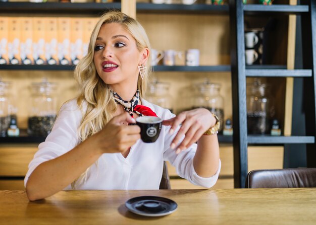 Blonde jeune femme assise dans le café tenant une tasse de café à la recherche de suite