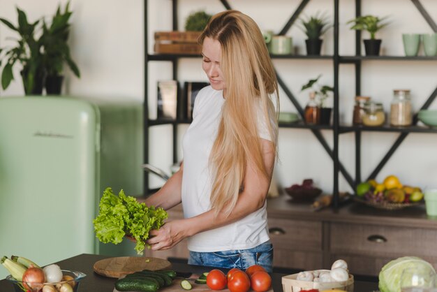 Blonde jeune femme debout dans la cuisine tenant la laitue