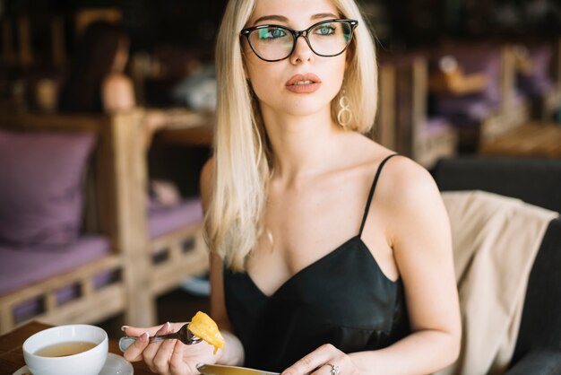 Blonde jeune femme portant des lunettes, manger de la nourriture dans le café