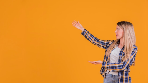 Blonde jeune femme présentant quelque chose sur un fond orange