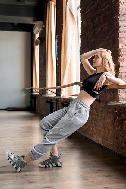 Blonde jeune femme se penchant sur la barre dans le studio de danse