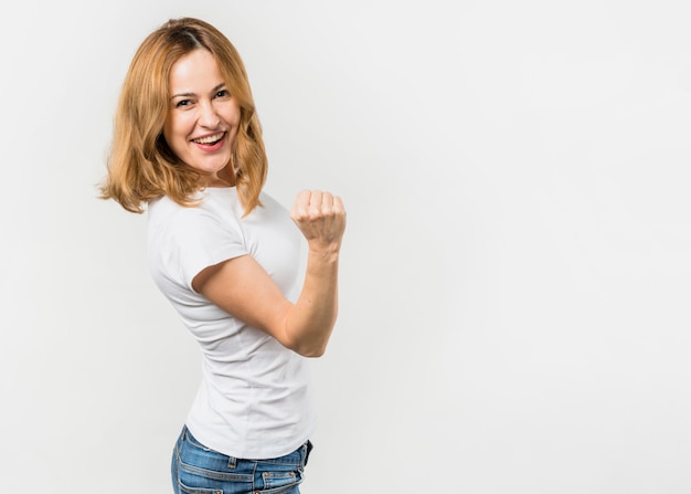 Blonde jeune femme serrant son poing debout contre un fond blanc