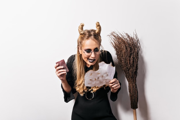 Blonde jeune sorcière à lunettes lecture sort. Portrait intérieur de l'assistant maléfique évoque à Halloween.