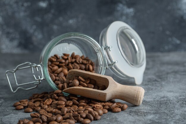 Un bocal en verre avec une cuillère en bois pleine de grains de café