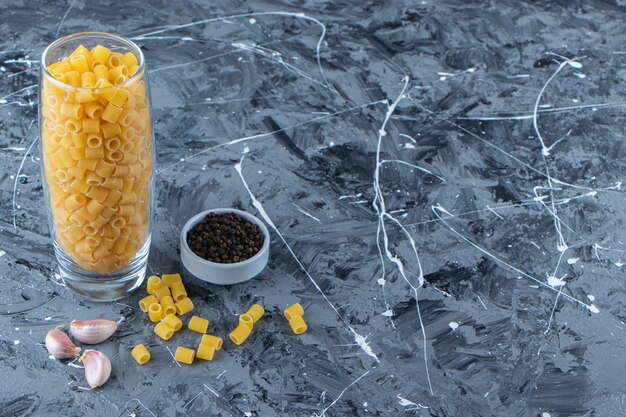 Un bocal en verre de spaghettis crus secs avec des grains d'ail et de poivre.