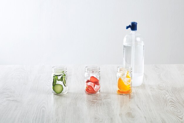 Bocaux rustiques avec de la glace et diverses garnitures. orange, fraise, concombre et menthe préparés pour faire de la limonade maison fraîche avec de l'eau pétillante de syphone.