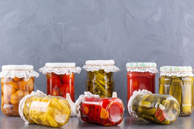 Bocaux en verre de concombres et tomates marinés sur table en pierre.