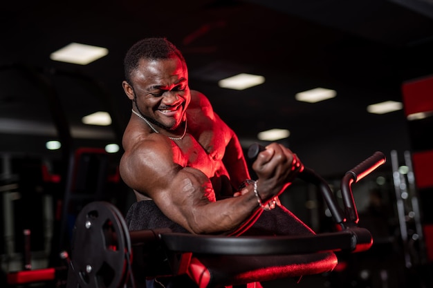 Bodybuilder afro-américain torse nu faisant du sport pour les mains. abdos forts. fond de salle de gym sombre. photo de côté.