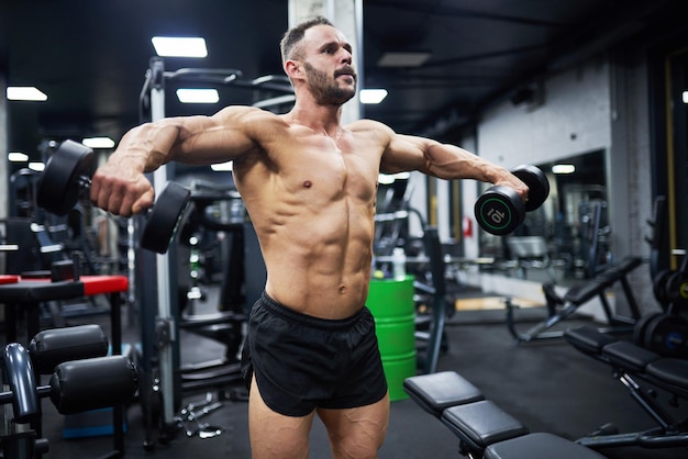 Un bodybuilder caucasien déterminé qui entraîne les muscles de la poitrine à l'aide d'haltères lourds.