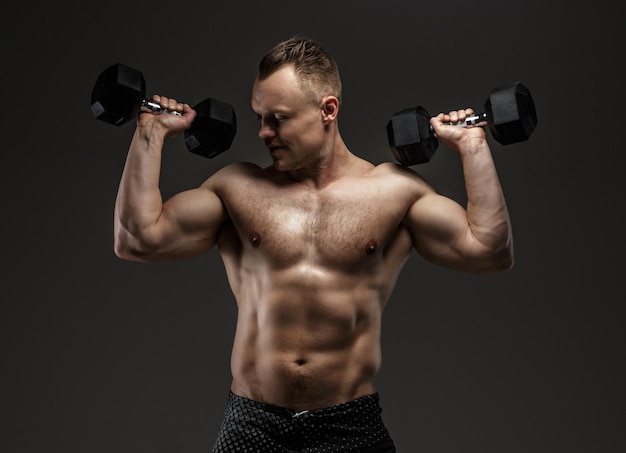 Bodybuilder en short noir tenant des haltères. Tournage en studio sur fond gris