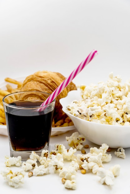 Boisson froide; paille; croissant avec bol de pop-corn sur table blanche