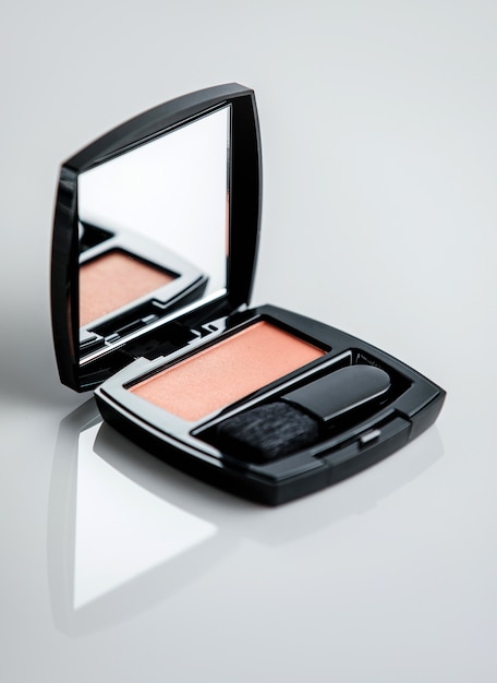 Une boîte de blush vue de face avec brosse et petit miroir sur la surface blanche