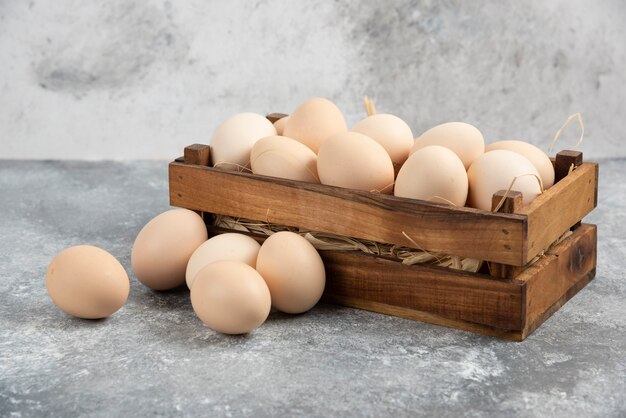 Boîte en bois d'oeufs crus biologiques sur une surface en marbre.