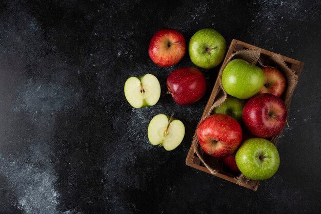 Boîte en bois de pommes biologiques fraîches sur une surface noire. .