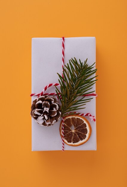 Boîte cadeau blanche décorée d'un ruban rouge, d'une branche de sapin, d'une pomme de pin et d'une tranche d'orange séchée