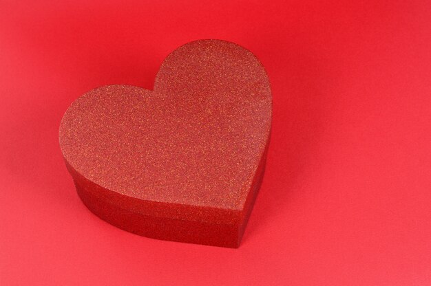 Boîte cadeau paillettes forme coeur sur fond de papier rouge.