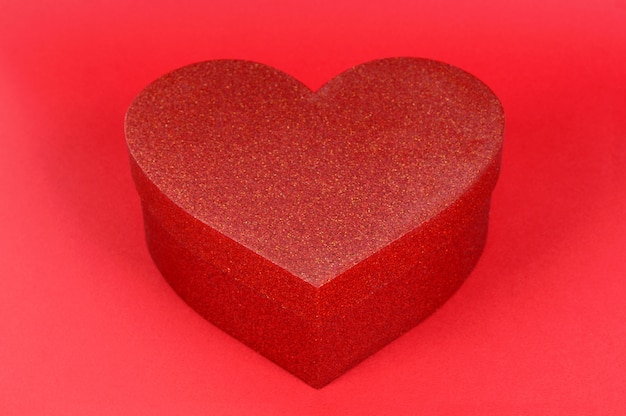 Boîte cadeau paillettes forme coeur sur fond de papier rouge.