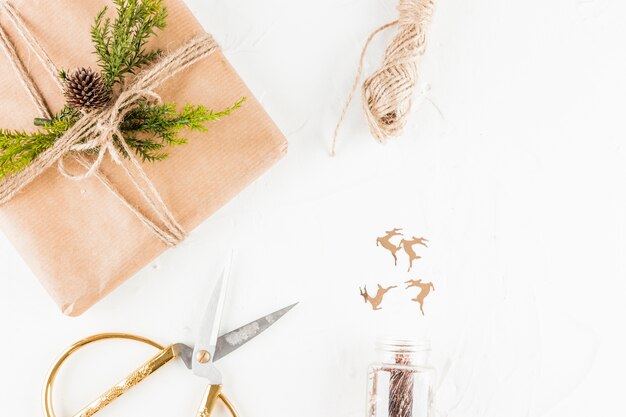 Boîte de cadeau en papier kraft avec une branche de conifère près des ciseaux