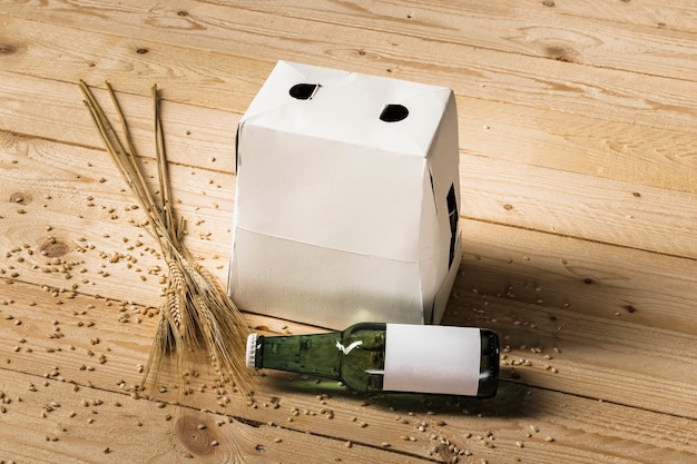 Boîte en carton; bouteille de bière verte et épis de blé sur une planche en bois