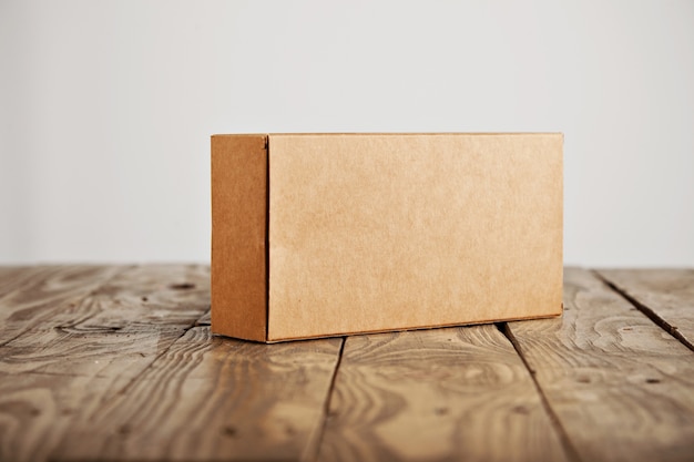 Boîte d'emballage en carton sans étiquette artisanale présentée sur table en bois brossé stressé, isolé sur fond blanc