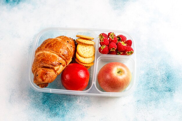 Boîte à lunch avec croissant frais, craquelins, fruits et framboises.