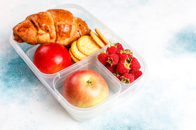 Photo gratuite boîte à lunch avec croissant frais, craquelins, fruits et framboises.