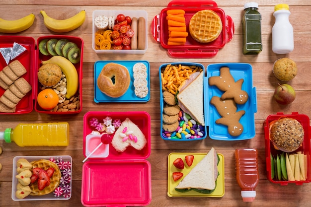 Boîte à lunch avec divers casse-croûte, des fruits et des aliments sucrés sur la table en bois