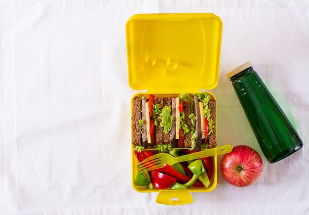 Boîte à lunch école saine avec sandwich au boeuf et légumes frais, bouteille d'eau et fruits sur tableau blanc.