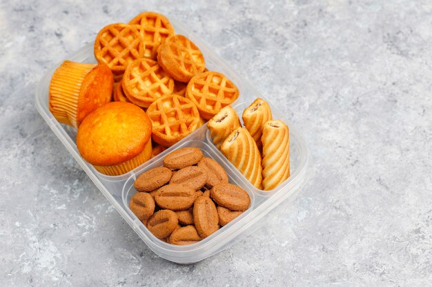 Boîte à lunch malsaine avec cookies, gaufres.muffins sur la surface en béton