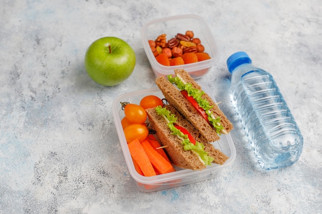 Boîte à lunch avec sandwich, légumes, fruits à blanc.