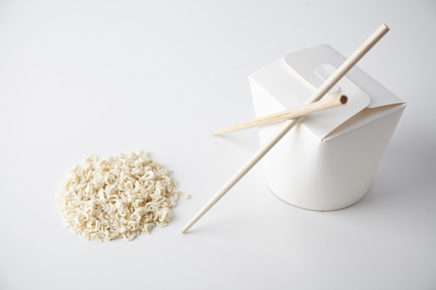 Boîte de nouilles à emporter vide fermé avec des baguettes près de pâtes sèches en forme de cercle isolé sur blanc présentation commerciale