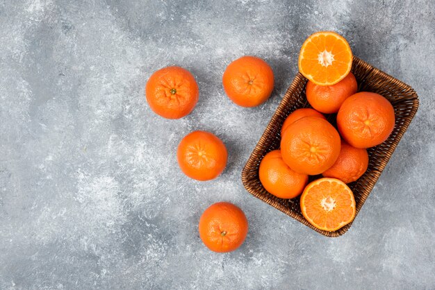 Une boîte en osier pleine de fruits orange juteux sur table en pierre.