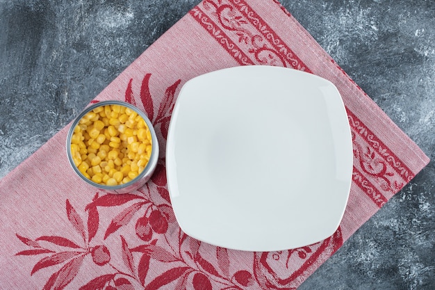 Une boîte pleine de graines de maïs soufflé avec une assiette vide sur une nappe.