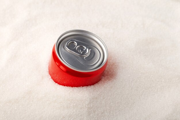 Boîte rouge de boisson gazeuse sucrée s'enfonçant dans un tas de sucre raffiné excès de sucre dans les boissons gazeuses