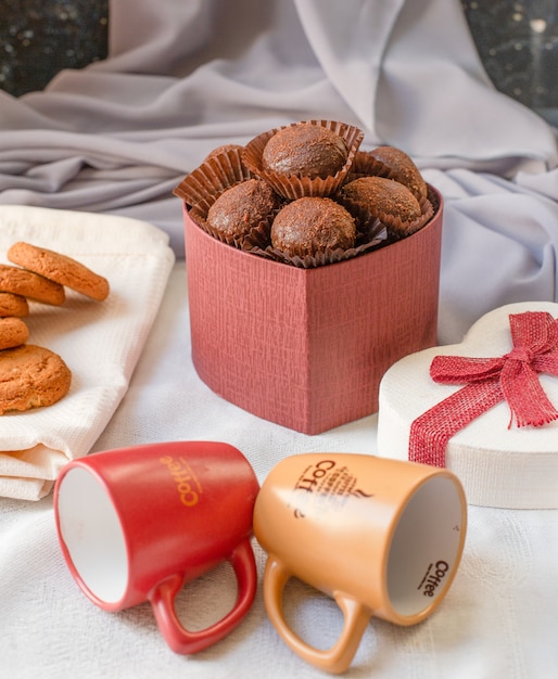 Une boîte rouge de pralines au chocolat avec des tasses de café vides sur la table.