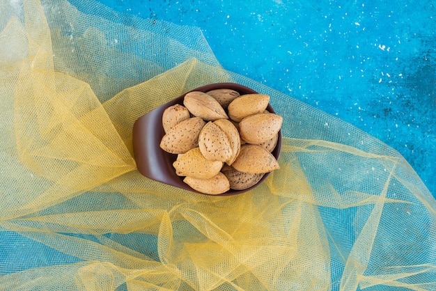 Un bol d'amandes décortiquées sur tulle, sur la table bleue.