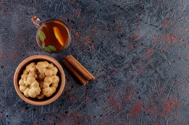 Un bol en argile de petits gâteaux ronds avec un trou et une tasse en verre de thé chaud.