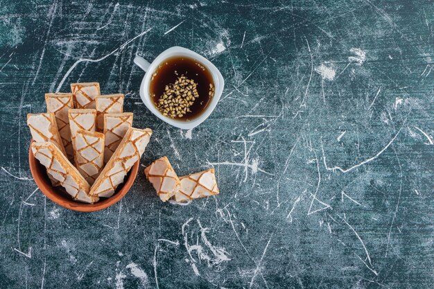 Un bol d'argile plein de bâtonnets de gaufres sucrées avec une tasse de thé noir.