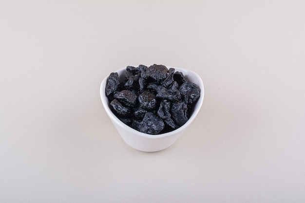 Bol blanc de fruits de prune séchés placés sur une surface blanche. Photo de haute qualité