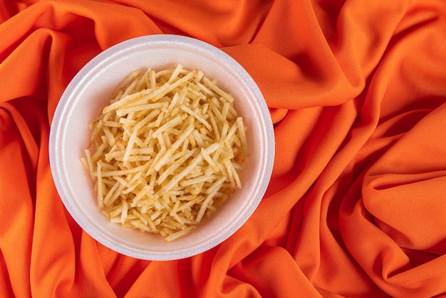 Photo gratuite bol blanc avec paille de pommes de terre sur surface orange