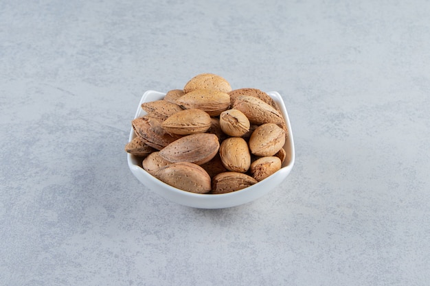 Bol blanc plein d'amandes décortiquées sur fond de pierre.