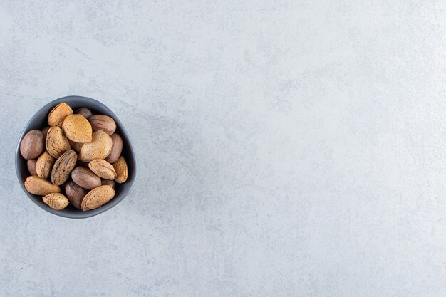 Bol bleu plein d'amandes et de noix décortiquées sur fond de pierre.