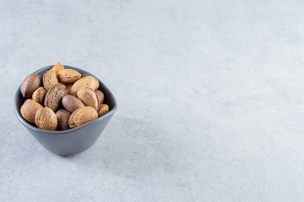 Bol bleu plein d'amandes et de noix décortiquées sur pierre.