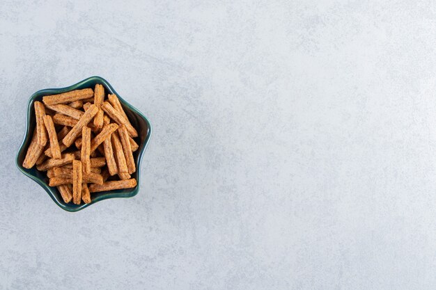 Bol bleu de savoureux crackers bâton sur fond de pierre.