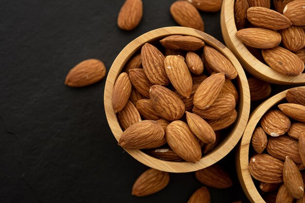 Bol en bois aux amandes sur fond noir. Vue de dessus.