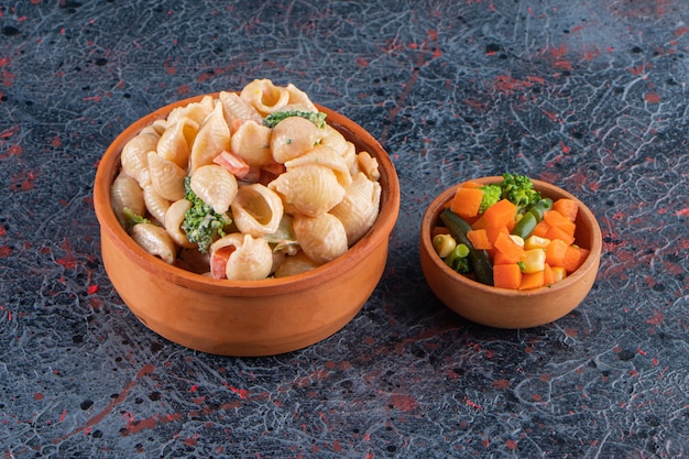 Bol en bois de délicieuses pâtes aux coquillages et mini salade sur une surface en marbre.