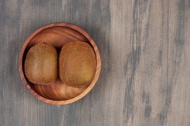 Un bol en bois avec deux kiwis frais sur une table en bois. Photo de haute qualité