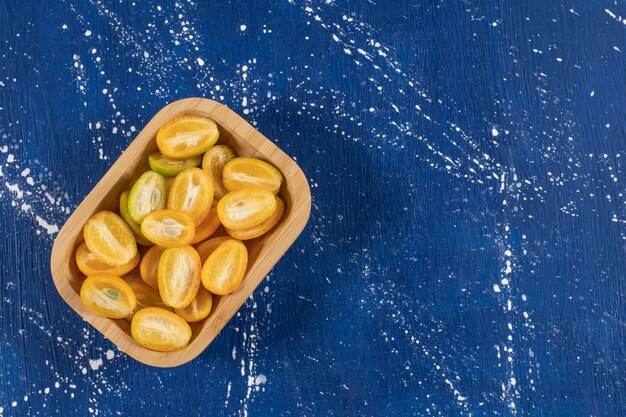 Photo gratuite bol en bois de fruits frais tranchés de kumquat sur une surface en marbre.