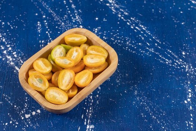 Bol en bois de fruits frais tranchés de kumquat sur une surface en marbre